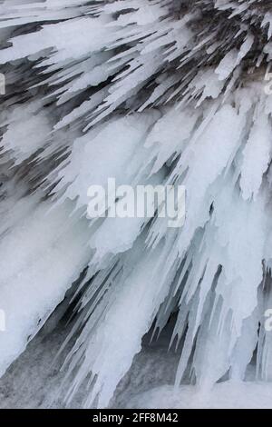 The rock on the frozen lake Baikal is covered with a thick layer of blue ice: many icicles and splashes Stock Photo