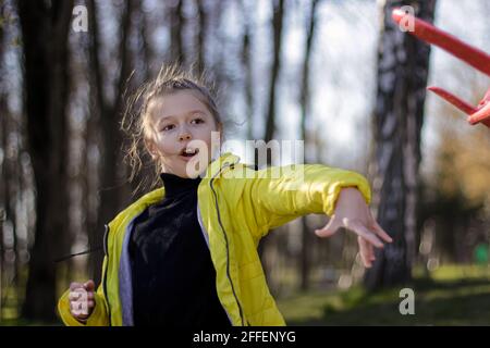 Kid girl throwing a toy plane to flying on air in the nature garden. Side view. Stock Photo