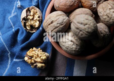 Shelled and cracked walnuts scattered from the bowl on a blue and brown cotton kitchen cloth were photographed in dark mode. Close up Stock Photo