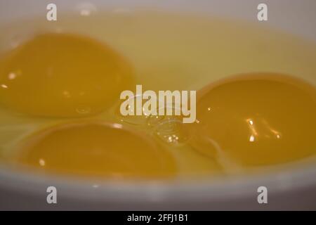 three raw eggs cracked into a plain white bowl Stock Photo