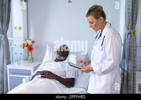 Caucasian female doctor standing next to african american male in hospital patient room using tablet Stock Photo