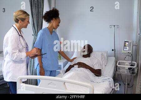 Two diverse female doctors and african american male patient in hospital room smiling to each other Stock Photo