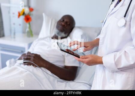 Caucasian female doctor standing next to african american male in hospital patient room using tablet Stock Photo