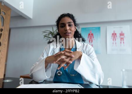 Mixed race female doctor at desk talking and gesturing during video call consultation