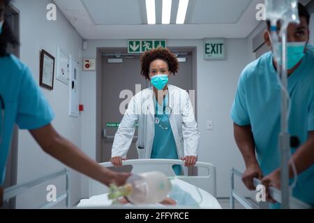 Mixed race doctors wearing face masks transporting patient in hospital bed Stock Photo
