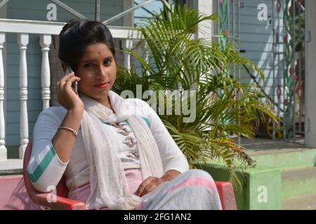 Teenage Indian Bengali girl sitting on a chair talking in mobile phone, selective focusing Stock Photo