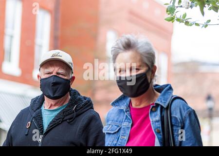 Easton, MD, USA 04-16-2021: An elderly caucasian couple wearing casual clothes, hat and cloth face mask is walking on the street during COVID-19 pande Stock Photo