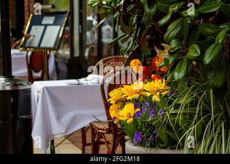 Out of focus outdoor restaurant tables with decorative flowers in focus. Abstract Concept image for outdoor dining with outside seating on spring or s Stock Photo