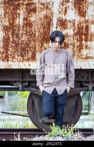 Portrait of smiling handsome Asian man standing at public train station. Young Man Standing in Old Vintage Train Stock Photo