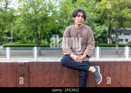 handsome young man sitting outside on train tracks and looking pensive Stock Photo