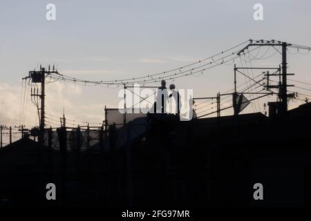 Workers on roof under electrical wires at sunset Stock Photo