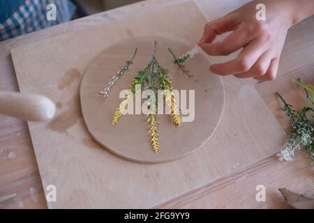 Senior female artisan creating handmade ceramics in pottery studio making composition of flowers on plate. Stock Photo