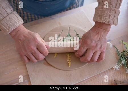 Senior female artisan creating handmade ceramics in pottery studio making composition of flowers on plate. Stock Photo