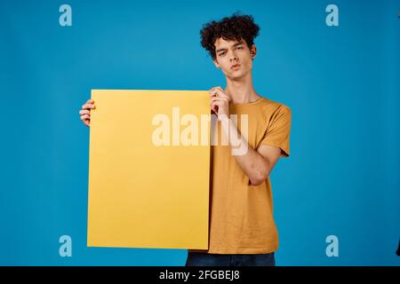 guy with curly hair yellow posters in hands Copy Space blue background studio Stock Photo