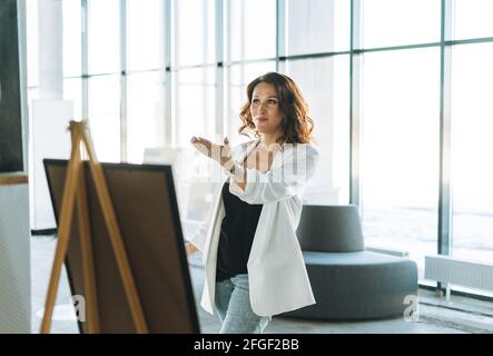 Charming brunette young woman in white suit visits the modern art gallery exhibition Stock Photo
