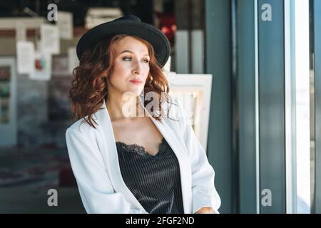 Charming young woman businesswoman in black felt hat and white suit visits the modern art gallery exhibition Stock Photo