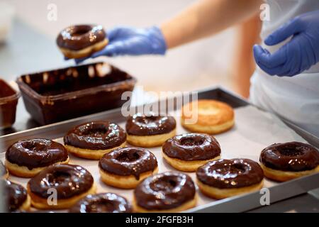 Chocolate topping on donuts in a working atmosphere in a candy workshop. Pastry, dessert, sweet, making Stock Photo