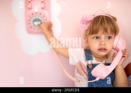 A little girl is playing with a retro phone on the wall of a pastry shop in a pleasant atmosphere. Pastry shop, dessert, sweet Stock Photo