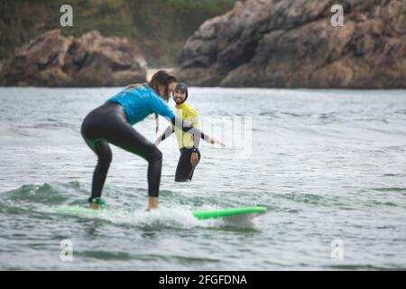 Galicia, Spain - August 2, 2020: Surf lessons on the beach of San Antonio, Espasante. Novice surfers, learning with their surfboards on a cloudy day, Stock Photo