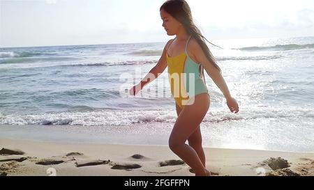 Adorable little girl in swimsuit listening to sea shell on white
