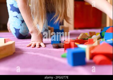 a kid girl of seven years old plays at home with toys, wooden building blocks, during quarantine self isolation covid-19 corona virus Stock Photo