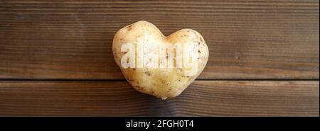 ugly food. an ugly vegetable a heart shaped potato on a wooden plank table. banner Stock Photo