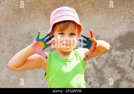 Happy young little school age child, girl holding up both her hands covered in colorful paint, outdoors portrait, lifestyle shot Children and art, cre Stock Photo