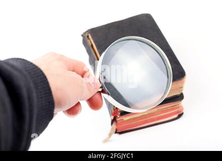 Man holding a loupe, magnifying glass in hand inspecting small old antique books, taking a closer look. Archival historical literature examination, an Stock Photo
