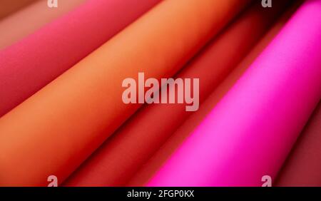 Online sale, offline selling, tailor or atelier concept. Close-up multicolored fabrics rolls in pink, orange, red colors. Fabrics retail store, drapery or textile shop. High quality image Stock Photo