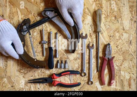 car drum brake disassembled in men's gloved hands and a set of various repair hand tools or auto mechanic's tools kit on a sheet of osb plywood backgr Stock Photo