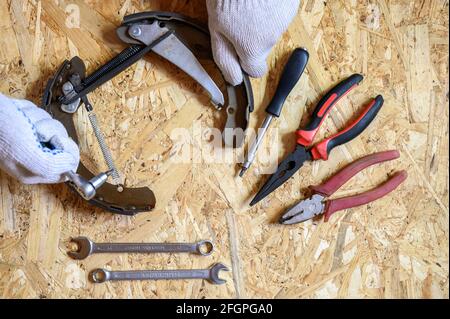 car drum brake disassembled in men's gloved hands and a set of various repair hand tools or auto mechanic's tools kit on a sheet of osb plywood backgr Stock Photo