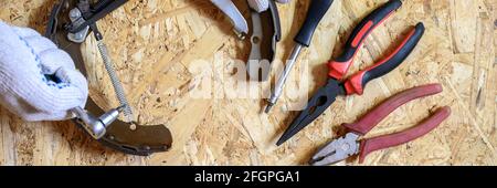 car drum brake disassembled in men's gloved hands and a set of various repair hand tools or auto mechanic's tools kit on a sheet of osb plywood backgr Stock Photo