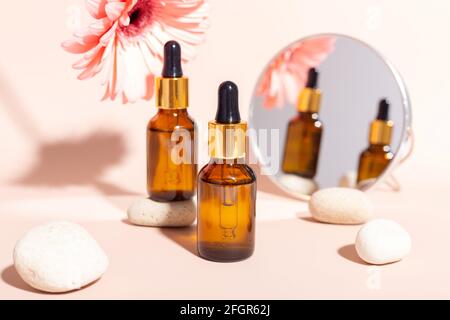 Set of facial serum in glass bottles with pipette, natural organic spa cosmetic. Pink gerbera flower. Skin care concept - Image Stock Photo