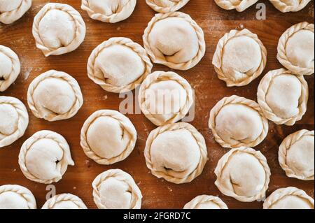 pile of small homemade uncooked dumplings with meat on kitchen table. national traditional Russian cuisine. do it yourself. top view, flat lay Stock Photo