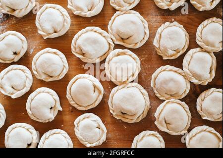 pile of small homemade uncooked dumplings with meat on kitchen table. national traditional Russian cuisine. do it yourself. top view, flet lay Stock Photo