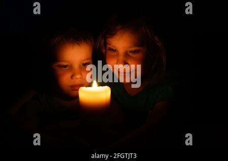 happy kids siblings boy and girl admires a burning wax candle in the evening at home Stock Photo