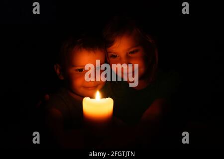 happy kids siblings boy and girl admires a burning wax candle in the evening at home Stock Photo