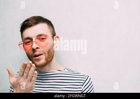 Young man in pink glasses sends a kiss. Valentine's day holiday. Light background. Stock Photo