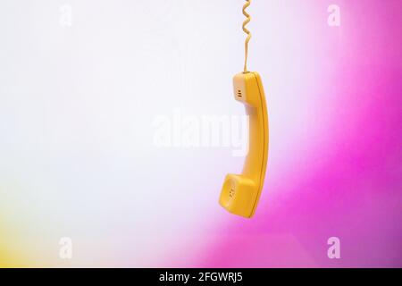 Telephone handset or receiver hanging from above on pinky background Stock Photo