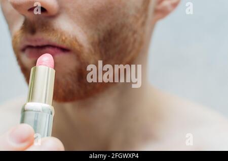 young man with a beard paints his lips with lipstick. Close-up. Stock Photo