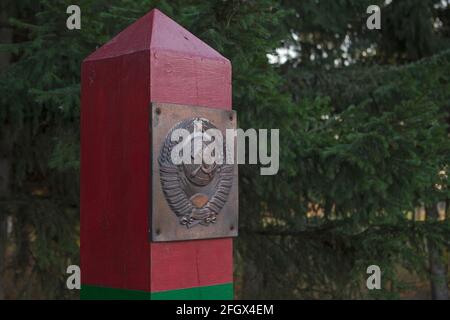 The top of wooden border post painted in green and red horizontal stripes with a metal plate depicting the coat of arms of the USSR attached in its to Stock Photo