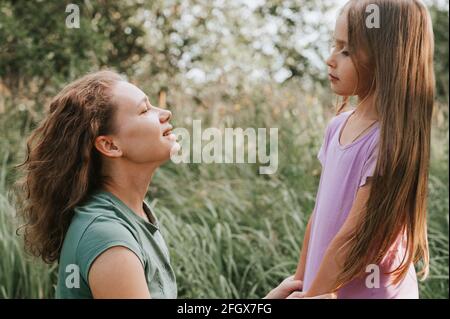 a mother with a small intra channel hearing aid communicates with her little daughter in nature outdoor Stock Photo