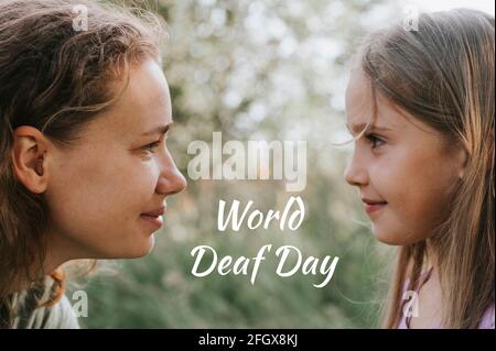 a mother with a small intra channel hearing aid communicates with her little daughter in nature outdoor. text 'World Deaf Day' OFL font Stock Photo