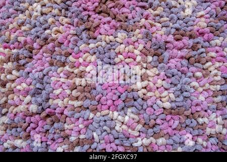 The surface of a multicolored rug knitted by a dense fluffy wool thread, which is an array of rounded loops of brown, pink, purple and beige colors. A Stock Photo