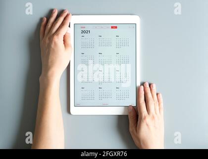 a tablet with an open calendar for 2021 year in a womans hands on a gray background Stock Photo