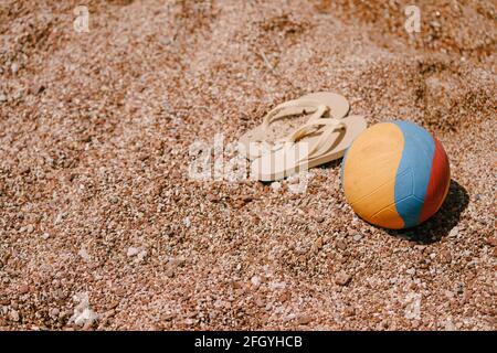 Multicolored ball and beige flip flops lie on the beach Stock Photo