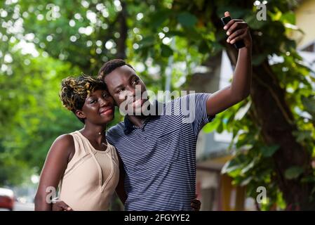 young couple standing in a park looking at mobile phone while smiling. Stock Photo