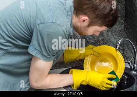 young guy washes a plate in the sink. Close-up. Concept man home cleaning Stock Photo