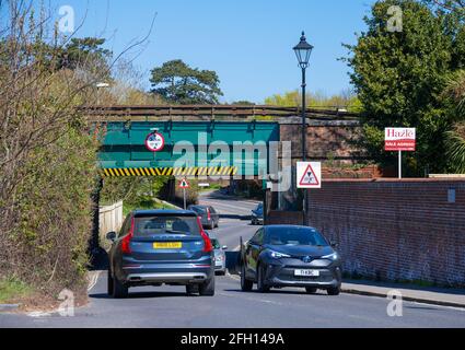 Cars and other vehicles driving on a British road under a low railway bridge with a height restriction sign in Emsworth, Hampshire, England, UK. Stock Photo