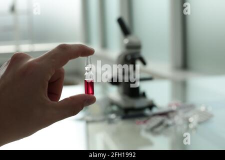 Doctor's hand holding a vaccine in his hands on the background of a glass table with medicines and a microscope Stock Photo